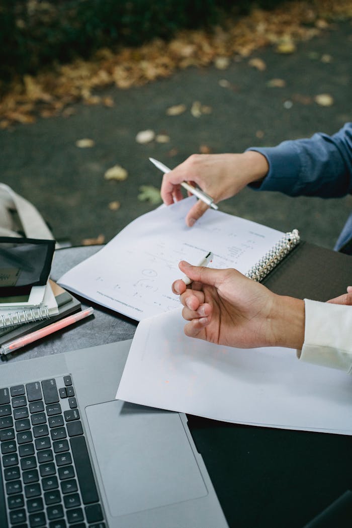High angle of crop anonymous male students using laptop while working with papers for studies