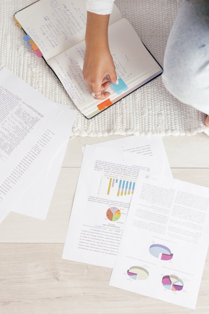 A young adult arranging study papers and notes with colorful tabs on a notebook, focusing on education and research.